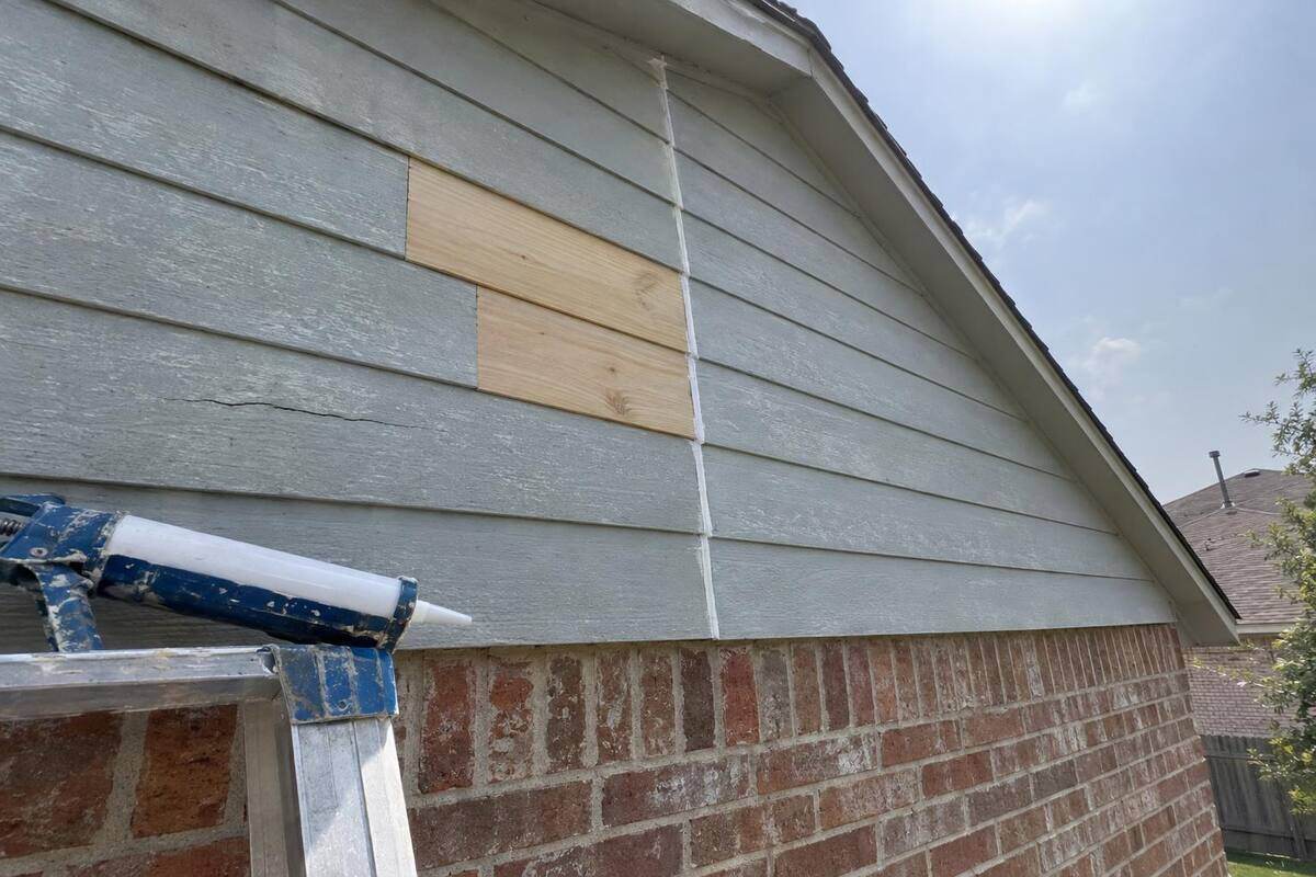 Freshly painted fiber cement lap siding on the gable of a two-story house, a new plank visible among the older ones