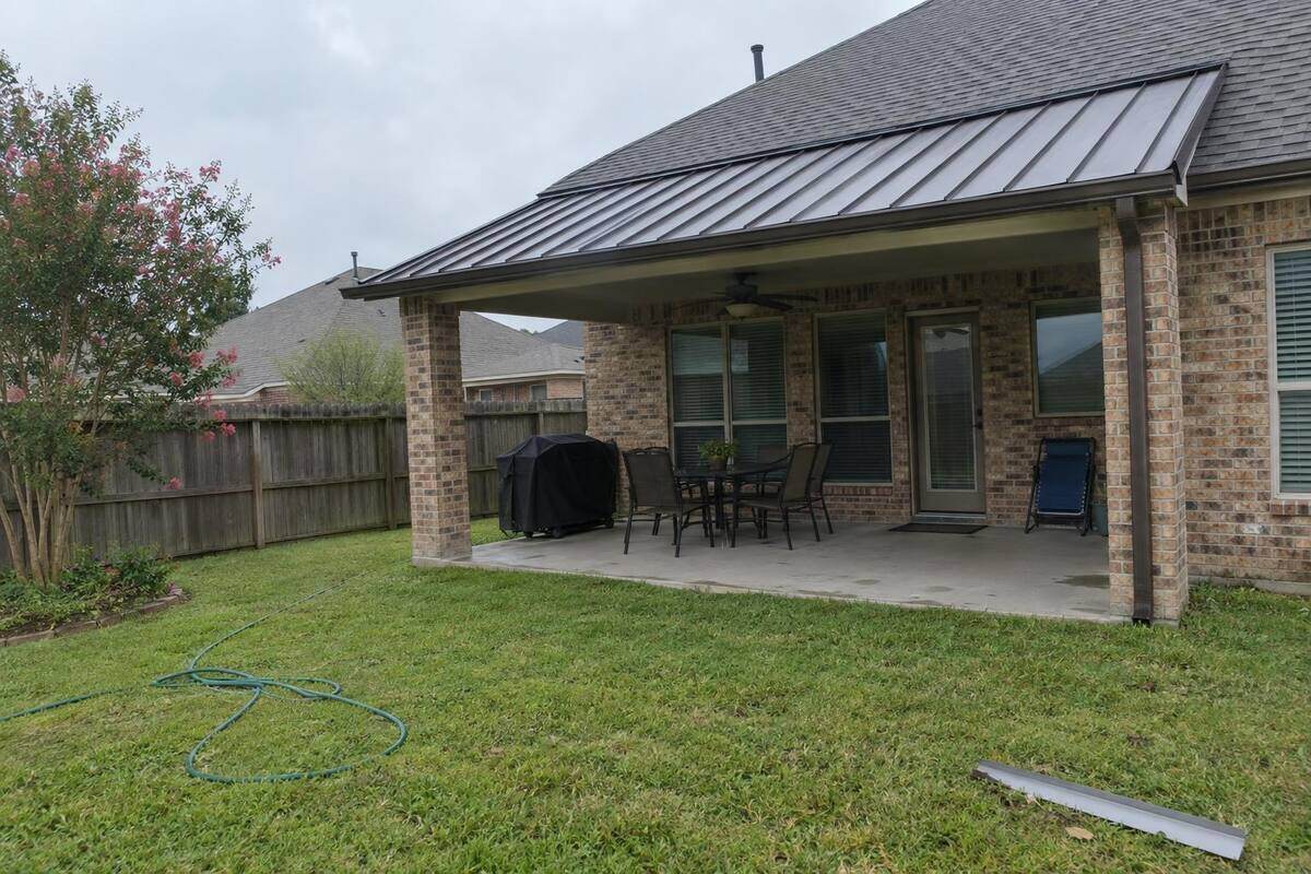 Dark standing-seam metal roof over a back porch attached to a brick Pearland house, a ceiling fan visible under the eave