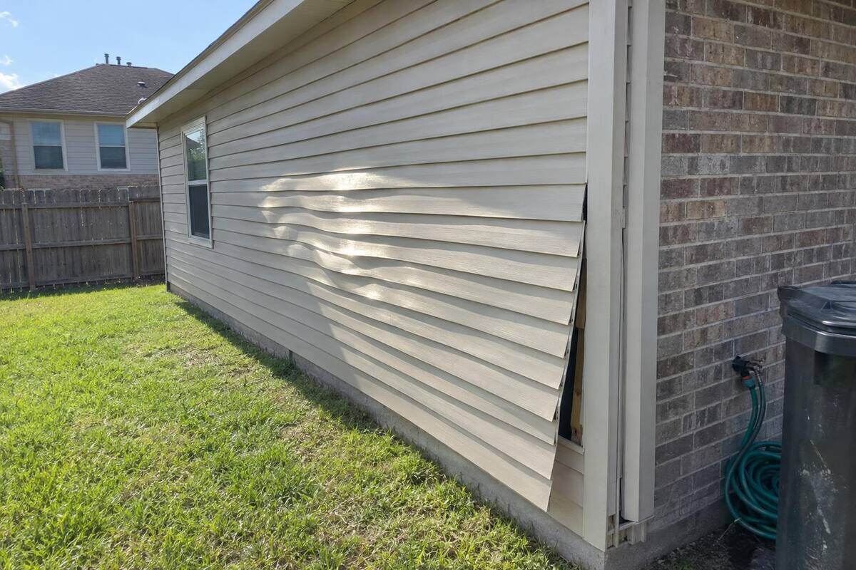 Beige vinyl lap siding on the side wall of a single-story addition, with one wavy, distorted section